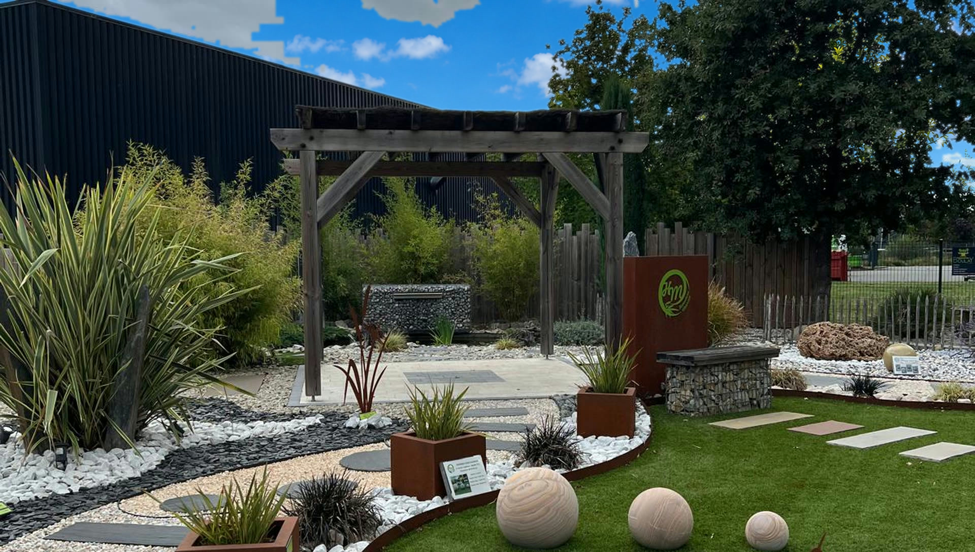 Pergola en bois au cœur d'un jardin d'exposition avec bordures Corten et sphères décoratives